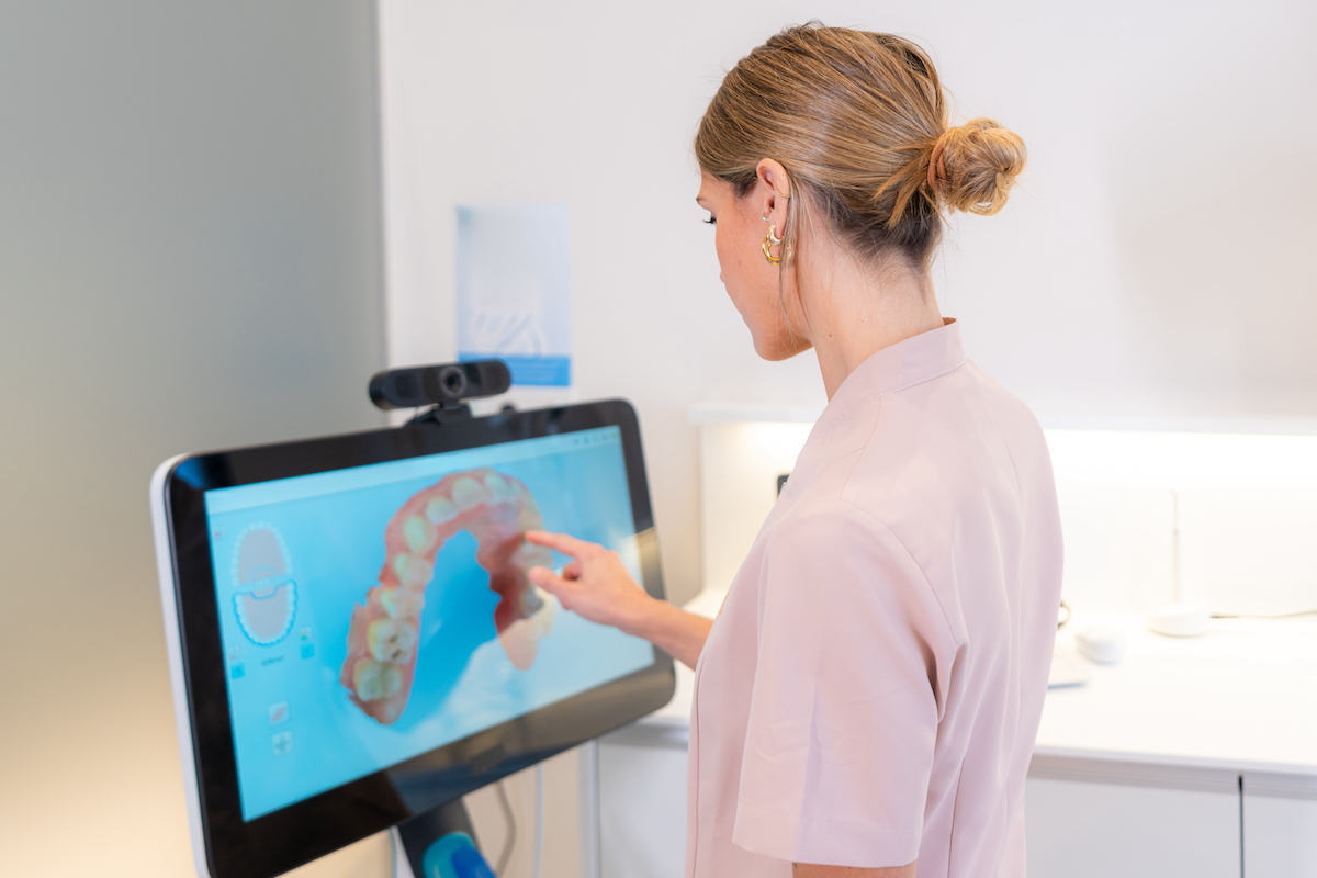 A dentist in a pink uniform interacts with a touchscreen displaying a 3D dental model, showcasing how AI is revolutionizing dental care.